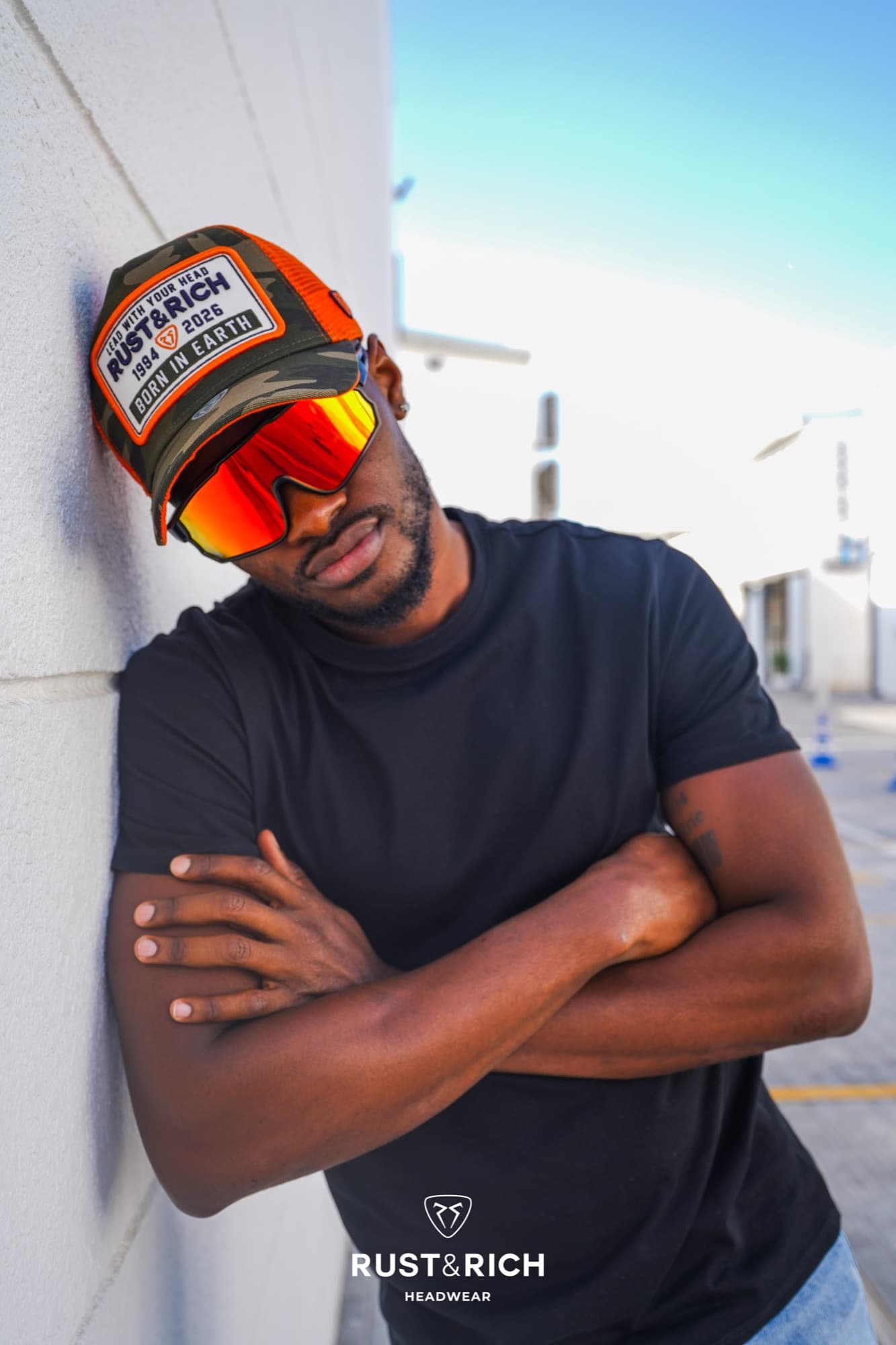 Rust and Rich campaign portrait leaning on a wall in a cap and red sunglasses